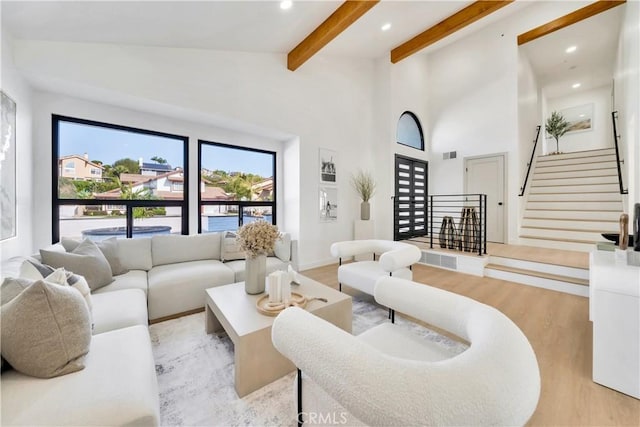 living room featuring a high ceiling, light hardwood / wood-style flooring, and beam ceiling