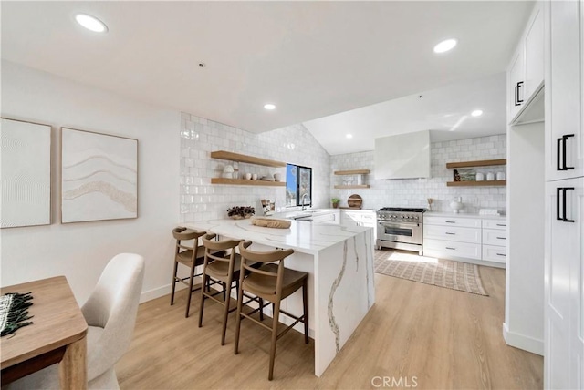 kitchen with a kitchen breakfast bar, kitchen peninsula, high end stainless steel range oven, wall chimney exhaust hood, and white cabinetry