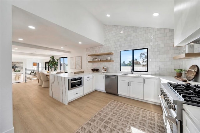 kitchen with kitchen peninsula, stainless steel appliances, light hardwood / wood-style floors, backsplash, and white cabinetry