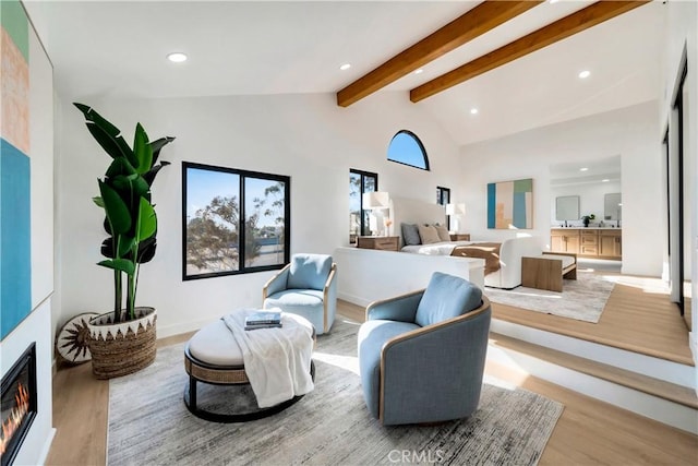 living room featuring high vaulted ceiling, light wood-type flooring, and beam ceiling