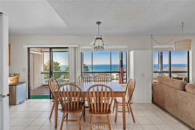 tiled dining area featuring a textured ceiling, a water view, and an inviting chandelier