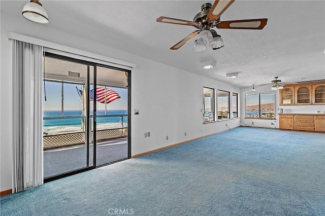 unfurnished living room featuring carpet floors, ceiling fan, and a water view