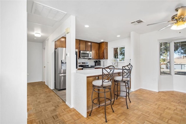 kitchen with appliances with stainless steel finishes, a kitchen breakfast bar, light parquet floors, ceiling fan, and kitchen peninsula