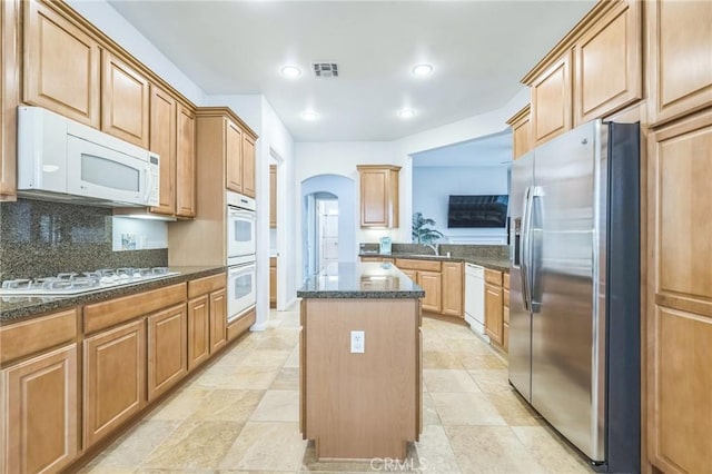 kitchen with sink, backsplash, dark stone counters, white appliances, and a kitchen island