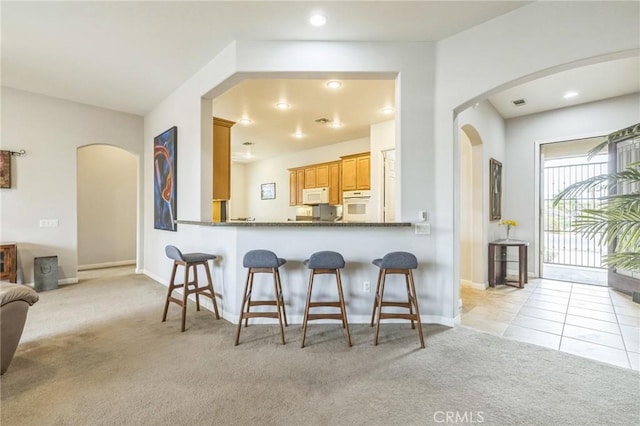 kitchen with a kitchen bar, white appliances, light colored carpet, and kitchen peninsula