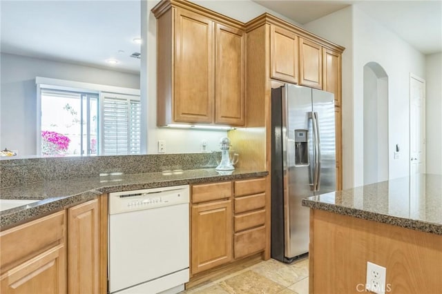 kitchen with stainless steel fridge, white dishwasher, and dark stone counters