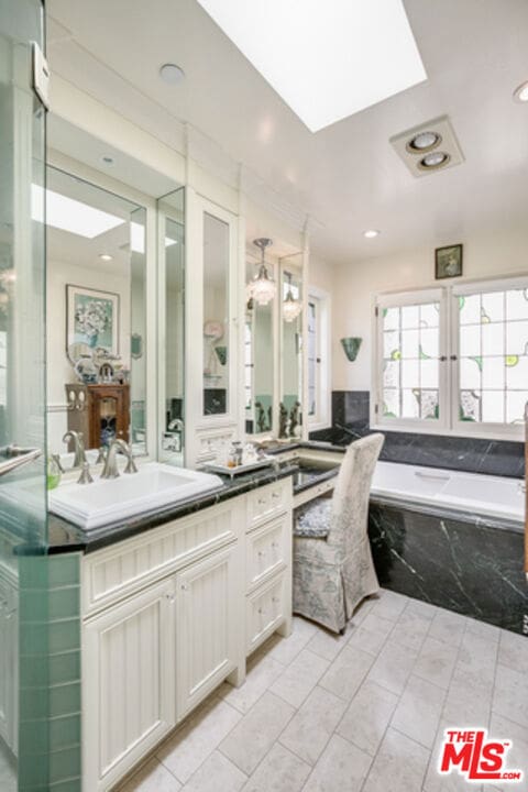 bathroom with a relaxing tiled tub, vanity, and a skylight