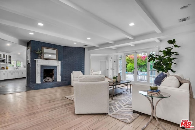 living room with light hardwood / wood-style flooring, beamed ceiling, and a brick fireplace