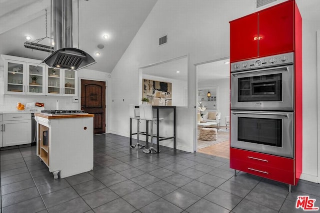 kitchen featuring island exhaust hood, appliances with stainless steel finishes, high vaulted ceiling, white cabinetry, and butcher block counters