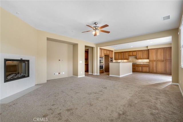 unfurnished living room featuring ceiling fan, a fireplace with flush hearth, visible vents, and light colored carpet