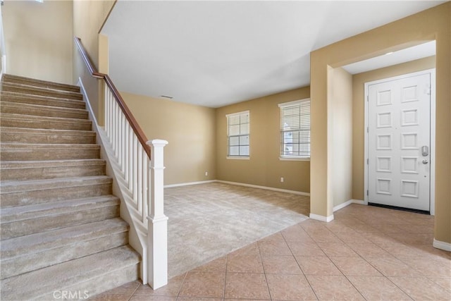 entryway with stairway, baseboards, light carpet, and light tile patterned floors
