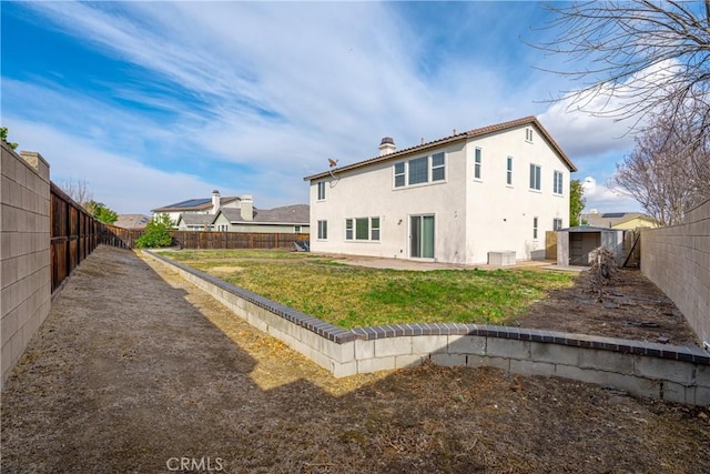 rear view of house featuring a lawn, a fenced backyard, a chimney, a patio area, and stucco siding