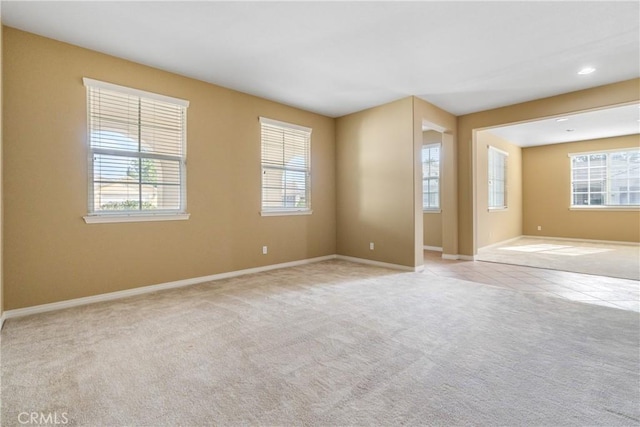 empty room with baseboards, a healthy amount of sunlight, light tile patterned flooring, and light colored carpet