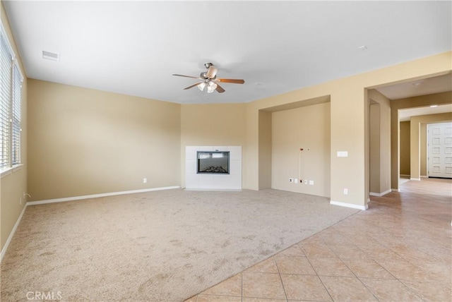 unfurnished living room with a tiled fireplace, light carpet, ceiling fan, light tile patterned flooring, and baseboards