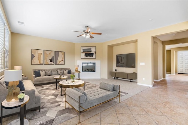 living room with light tile patterned floors, visible vents, baseboards, a glass covered fireplace, and ceiling fan