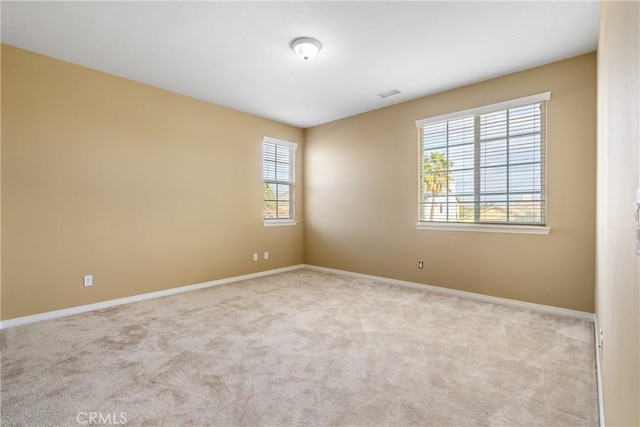 empty room featuring light carpet, visible vents, and baseboards