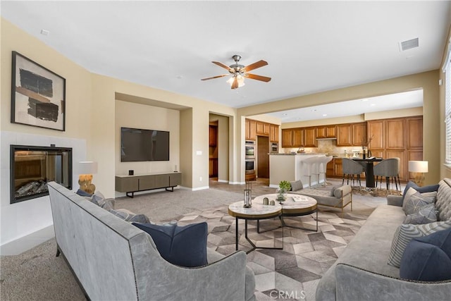 living room with ceiling fan, light carpet, a fireplace, visible vents, and baseboards