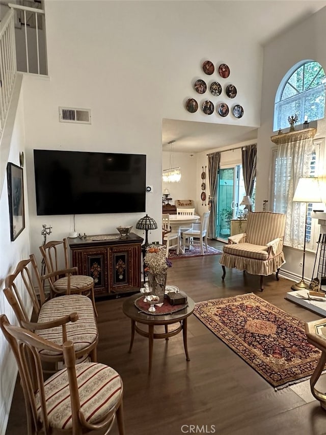 living room featuring dark wood-type flooring, a high ceiling, and a notable chandelier