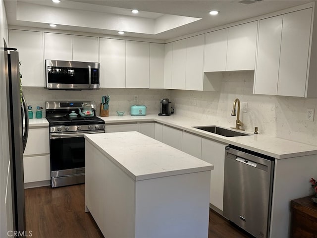 kitchen featuring appliances with stainless steel finishes, dark wood-type flooring, sink, white cabinets, and a center island