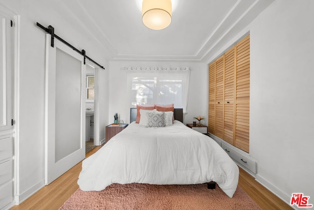 bedroom with a barn door, light hardwood / wood-style floors, ensuite bath, and a closet