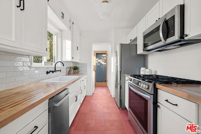 kitchen with wood counters, appliances with stainless steel finishes, decorative backsplash, sink, and white cabinetry