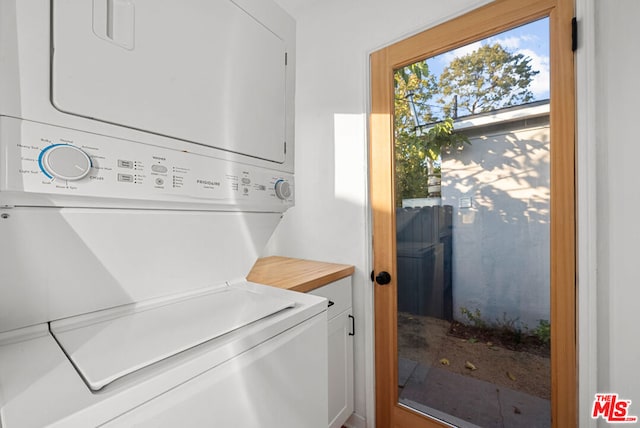 clothes washing area with cabinets and stacked washer and clothes dryer