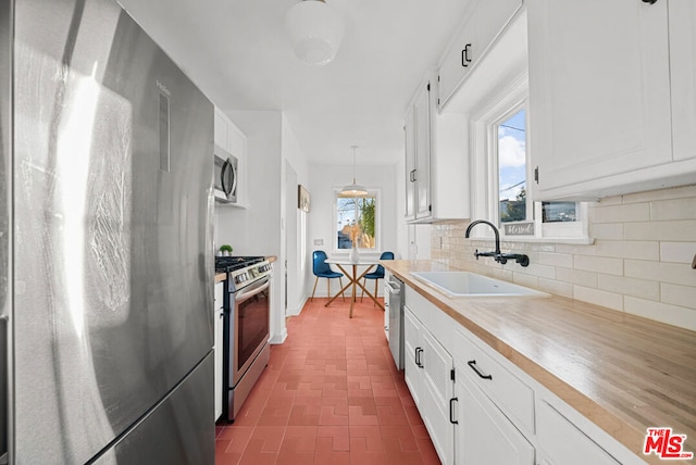 kitchen with decorative backsplash, stainless steel appliances, sink, decorative light fixtures, and white cabinets