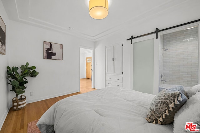 bedroom featuring a barn door, ensuite bathroom, and light hardwood / wood-style floors