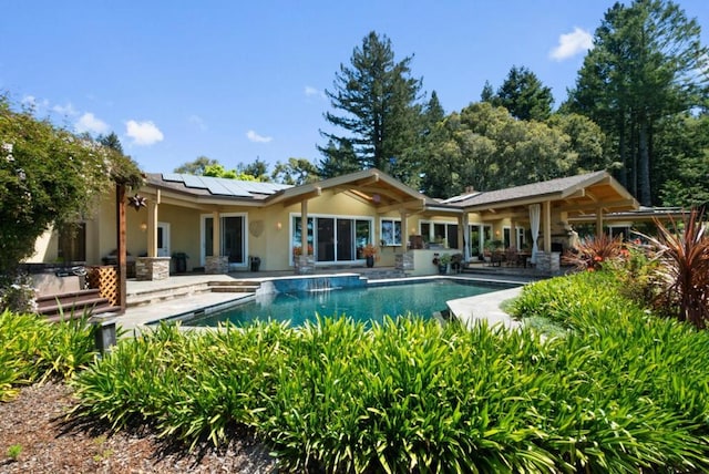 back of property featuring a patio area, a pool with hot tub, and solar panels