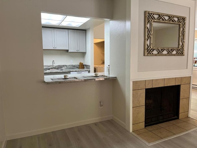 kitchen featuring light wood-type flooring, a tiled fireplace, washing machine and dryer, and sink