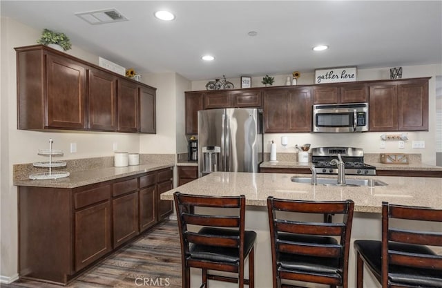 kitchen with dark hardwood / wood-style flooring, light stone counters, dark brown cabinetry, stainless steel appliances, and sink