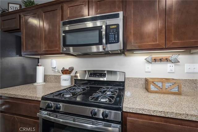 kitchen featuring dark brown cabinets, light stone counters, and stainless steel appliances