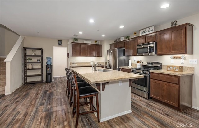 kitchen featuring a breakfast bar, stainless steel appliances, dark wood-type flooring, sink, and an island with sink