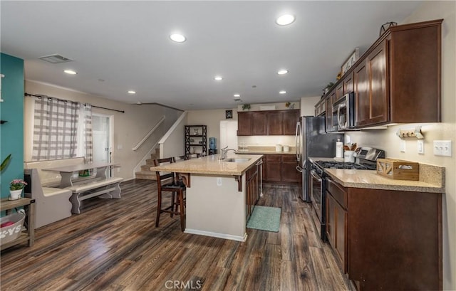 kitchen with a breakfast bar, appliances with stainless steel finishes, dark hardwood / wood-style flooring, and a center island with sink