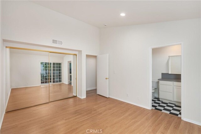 unfurnished bedroom featuring ensuite bath, a closet, and light wood-type flooring