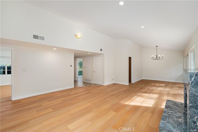 unfurnished living room with a notable chandelier, high vaulted ceiling, and light hardwood / wood-style flooring