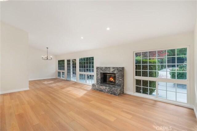 unfurnished living room with a high end fireplace, light hardwood / wood-style floors, and a notable chandelier