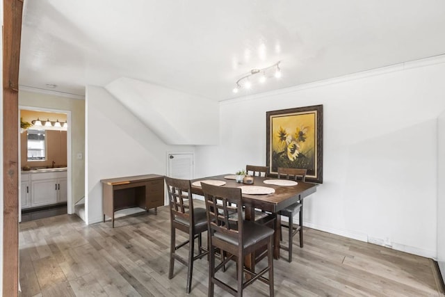 dining room featuring baseboards, wood finished floors, lofted ceiling, and crown molding