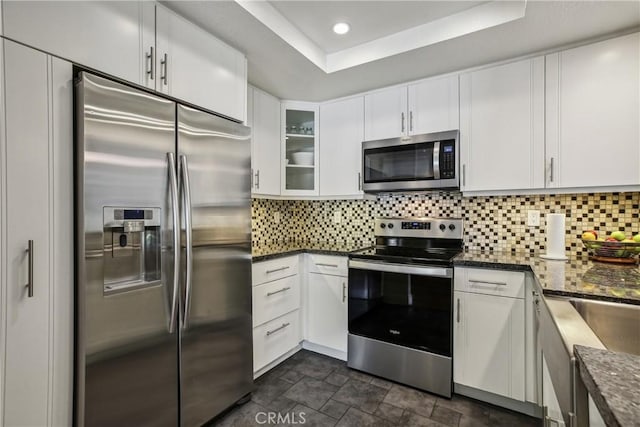 kitchen with white cabinetry, tasteful backsplash, dark stone counters, a tray ceiling, and appliances with stainless steel finishes