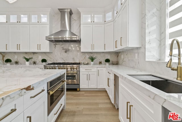 kitchen with decorative backsplash, white cabinetry, double oven range, and wall chimney range hood