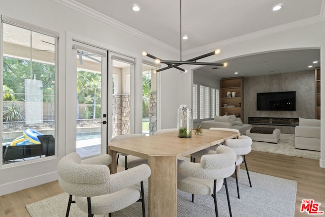 dining room with a high end fireplace, light wood-type flooring, crown molding, and a notable chandelier