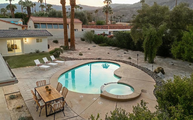 pool at dusk with a mountain view, a patio area, and an in ground hot tub