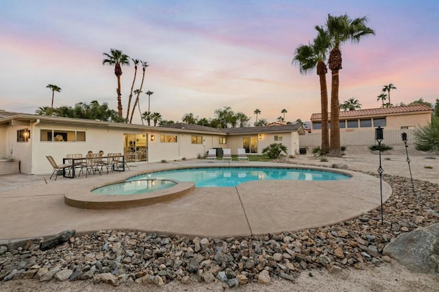 pool at dusk featuring an in ground hot tub and a patio