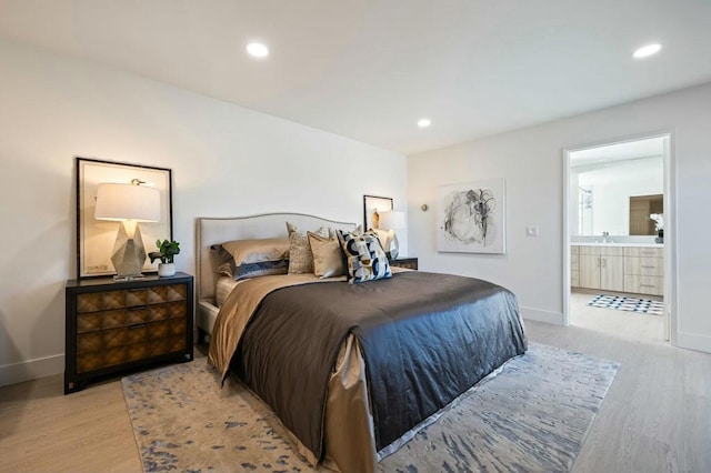 bedroom with light wood-type flooring, ensuite bathroom, and sink