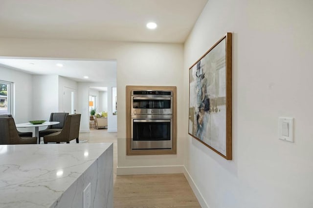 kitchen featuring light stone counters, light hardwood / wood-style flooring, and stainless steel double oven