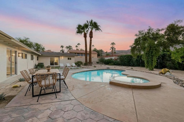 pool at dusk with an in ground hot tub and a patio