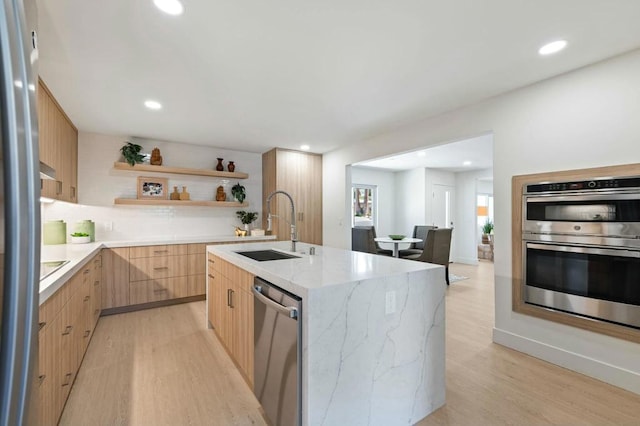 kitchen with a center island with sink, sink, light hardwood / wood-style flooring, light stone counters, and stainless steel appliances