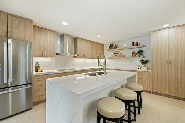 kitchen with stainless steel fridge, wall chimney exhaust hood, a kitchen island with sink, and light wood-type flooring