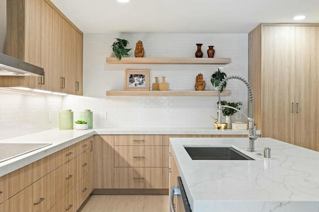 kitchen featuring wall chimney range hood, sink, light hardwood / wood-style flooring, tasteful backsplash, and light stone counters