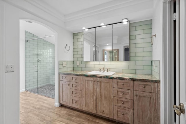 bathroom with wood-type flooring, decorative backsplash, a shower with door, vanity, and ornamental molding